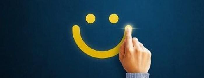Ein gelber Smiley wird von einer Hand auf einem dunkelblauen Hintergrund vervollständigt. Die Finger berühren den Punkt des Smileys, wodurch dieser zum Leuchten gebracht wird, was Freude vermittelt.