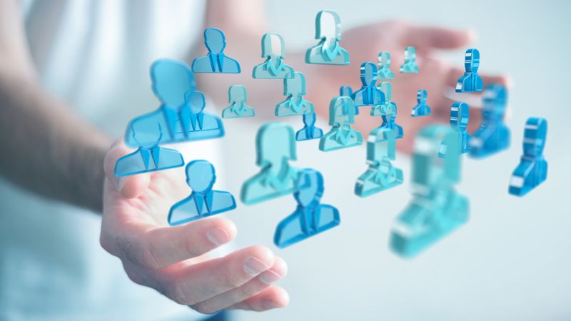 Transparente, blaue, stilisierte Figuren schweben vor zwei ausgestreckten Händen in einem diffusen, hellblauen Hintergrund. Die Figuren symbolisieren Menschen und wirken digital und abstrakt, repräsentierend vernetzte Kommunikation.