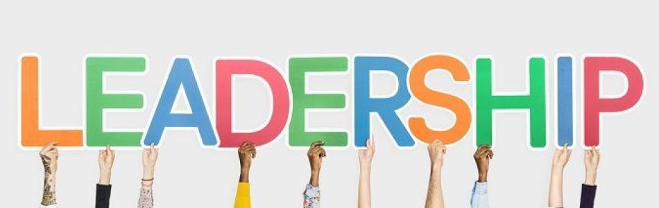 Mehrere Hände halten bunte Buchstaben hoch, die zusammen das Wort "LEADERSHIP" bilden. Die Buchstaben sind in unterschiedlichen Farben auf weißem Hintergrund gehalten. Die Hände reichen von unten und haben verschiedene Hauttöne.
